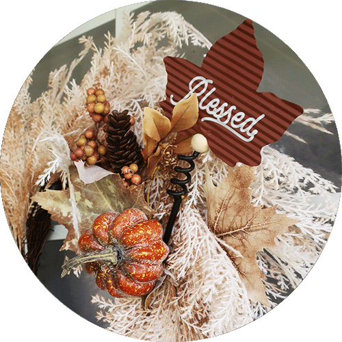 A white wreath with a fall floral picka nd a metal leaf pick.